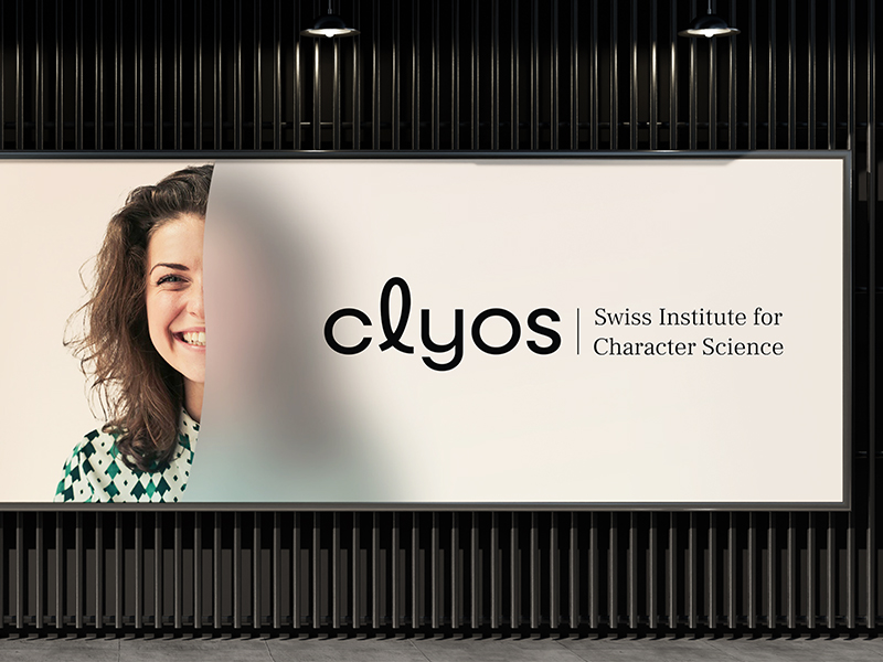 Großformatiges Markenbranding von clyos – Swiss Institute for Character Science mit halb sichtbarem Porträt einer Frau und klarer Typografie auf hellem Hintergrund vor dunkler Lamellenwand. Ein von Atelier Türke entwickeltes Branding und reduzierte, elegante Darstellung der Markenidentität.