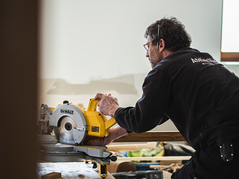 Ein Handwerker von Atelier Türke sägt ein Holzbrett mit einer Kreissäge in der Werkstatt.
