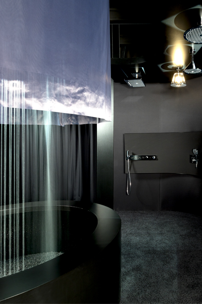 Reduzierter, dunkel gehaltener Showroom der Hansgrohe Aquademie Markenwelt mit rundem Wasserbecken und sanft herabfallendem „Powderrain“-Wasserregen, inszeniert durch gezielte Lichtakzente. Eine sinnliche Markenarchitektur, die das Element Wasser in den Mittelpunkt stellt und erlebbar macht, war Ziel der Inszentierung der Markenwelt von Atelier Türke.