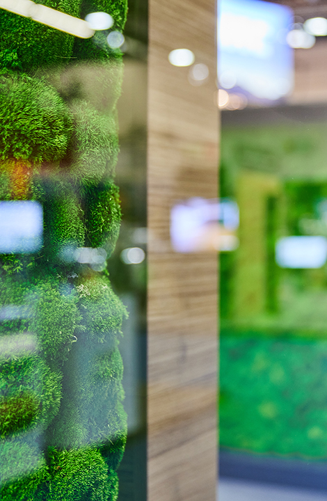 Detailaufnahme eines nachhaltigen Designelements mit bepflanzter, grüner Oberfläche, daneben Holzstruktur, in einem modernen Messe- oder Ausstellungsumfeld.