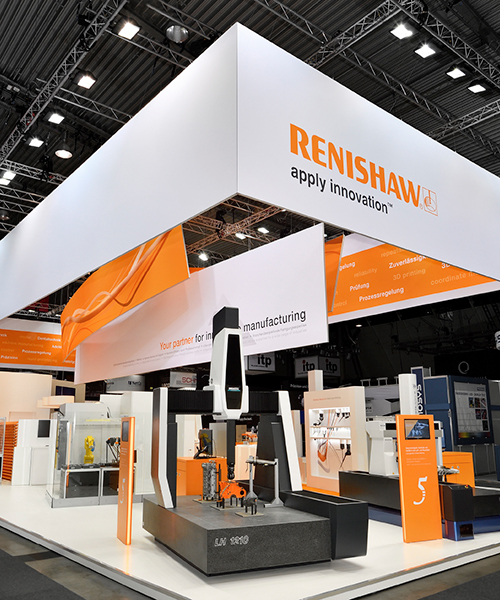 Messestand von Renishaw, entworfen und gebaut von Atelier Türke, in Orange und Weiß mit Maschinenexponaten und großflächiger Markenkommunikation in einer Messehalle.