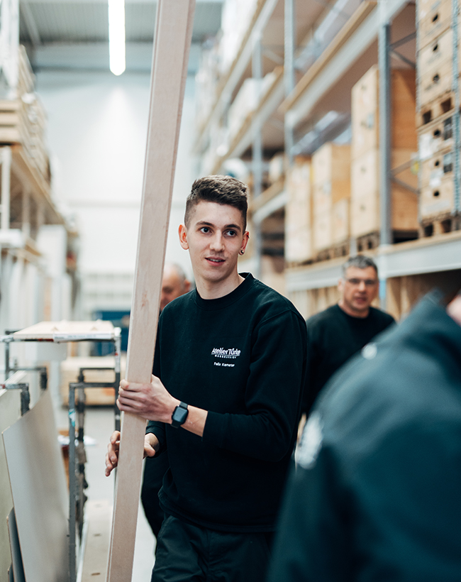 Felix Kemeter, Mitarbeiter im Lager und in der Montage bei Atelier Türke, beim Tragen einer Holzlatte
