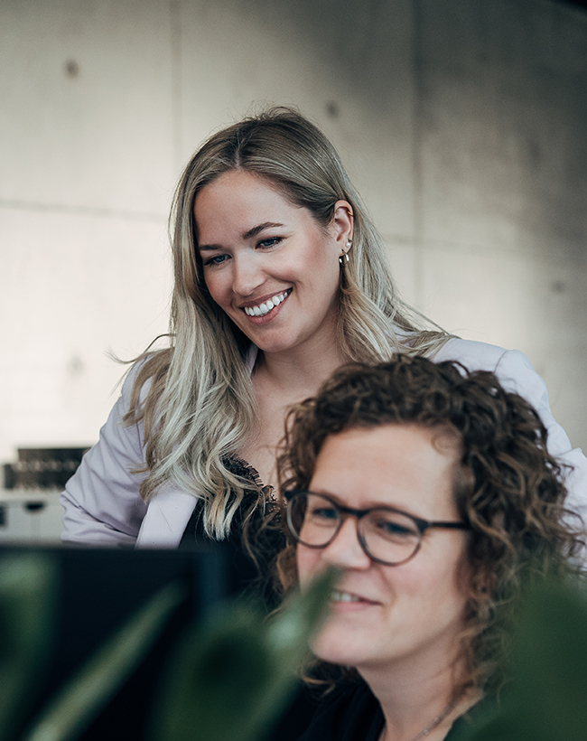 Lara Dohlenburg, Designerin für Messedesign und Innenarchitektur bei Atelier Türke, im Gespräch mit einer Kollegin vor dem PC